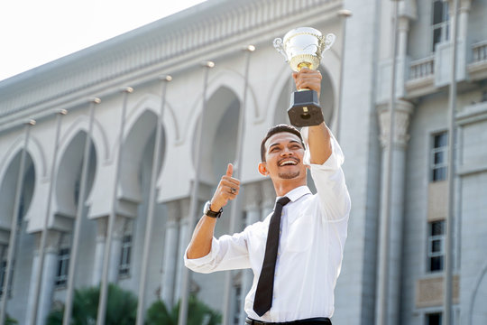 Young asian businessman Holding Trophy awards after successful with his business over a blur building background