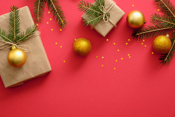 New year or Christmas frame border made of Christmas decorations, gold baubles, gift boxes wrapped kraft paper and fir tree branches on red background. Flat lay, top view, copy space
