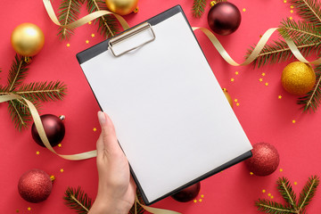 Hand holding clipboard mockup with blank paper over Christmas background with Christmas...