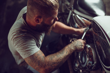 Handsome bearded man in leather jacket and sun glasses is sitting on the motorcycle in the repair...