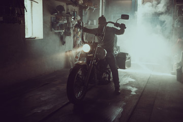Handsome brutal man with a beard sitting on a motorcycle in his garage
