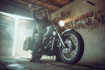 Handsome brutal man with a beard sitting on a motorcycle in his garage © toxicoz