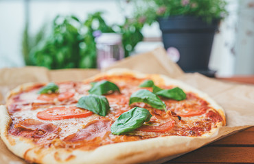 fresh homemade pizza with serrano ham, sliced tomatoes and fresh basil leaves on wooden table on patio