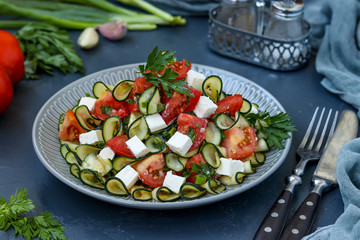 Healthy salad with zucchini, tomatoes and feta, dressed with olive oil in a plate on a dark background, horizontal orientation