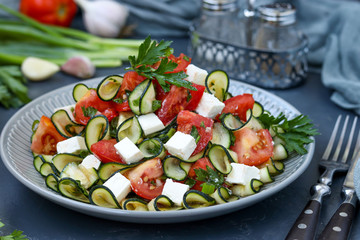 Healthy salad with zucchini, tomatoes and feta, dressed with olive oil in a plate on a dark background, horizontal orientation
