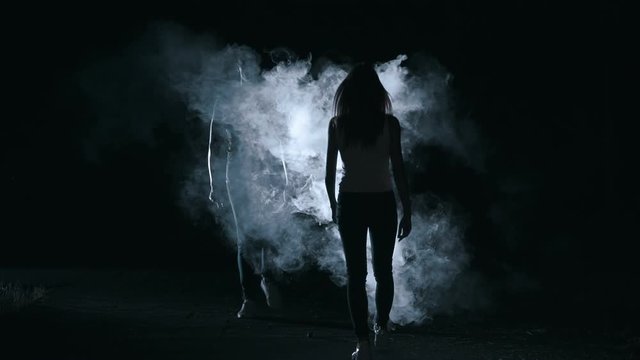 The woman and man walking through a smoke cloud in a dark background