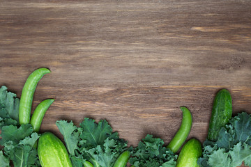 Frame from green salad leaves, peas, cucumbers on wooden background. Vegetables, vegan, harvest, recipe concept. Top view, copy space, flat lay, layout design