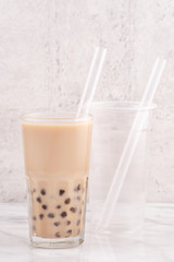 Tapioca pearl ball bubble milk tea, popular Taiwan drink, in drinking glass with straw on marble white table and wooden tray, close up, copy space.