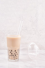 Tapioca pearl ball bubble milk tea, popular Taiwan drink, in drinking glass with straw on marble white table and wooden tray, close up, copy space.