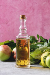 Bottle of apple vinegar with garden apples with leaves and branches on table with pink background. Autumn home harvesting.