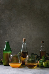 Variety of apple drinks. Bottles ang glasses of apple juice, vinegar and cider with garden apples with leaves and branches on table with dark background. Autumn home harvesting.