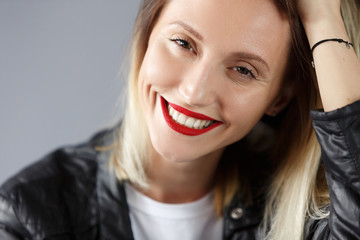 Obraz na płótnie Canvas Beautiful young woman blonde in leather jacket smiles and poses in the studio on the grey background. Place for text