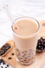 Tapioca pearl ball bubble milk tea, popular Taiwan drink, in drinking glass with straw on marble white table and wooden tray, close up, copy space.