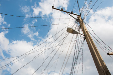 Obraz premium Electric pole with a street lamp and tangled electric cables with blue sky.