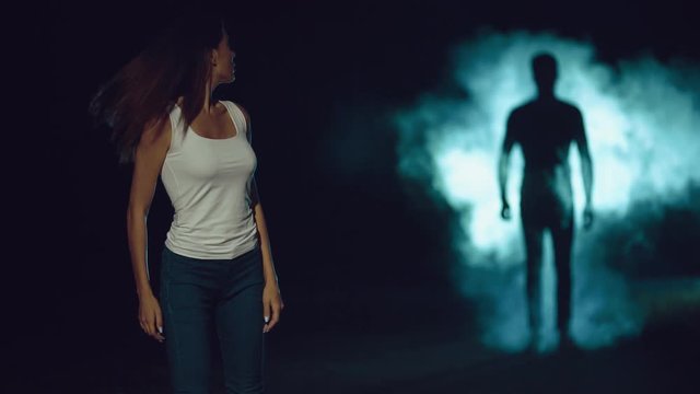 The woman walking in a dark street against the man silhouette in a smoke cloud