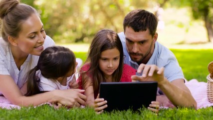 family, leisure and people concept - happy mother, father and two daughters with tablet computer lying on picnic blanket in summer park