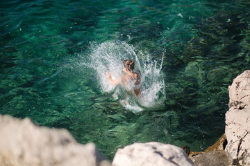 Young woman jump from the rock into the sea, water. Emotion and splash. Top view