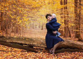 Mother and daughter in blue dresses sitting on a fallen tree in a yellow autumn forest