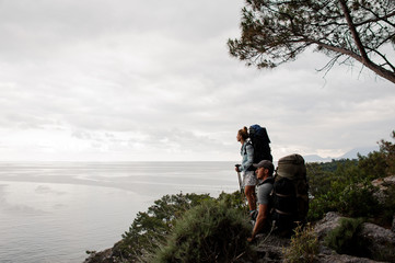Man and woman with backpacks standing on on the rock under the tree