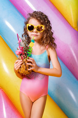 Pretty smiling girl wearing pink and blue swimwear and sunglasses holding pineapple cocktail with...