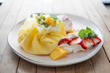 Crepe and ice cream with fresh fruit on wooden table.