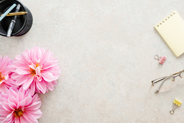 Flat lay home office desk. Female workspace with pink dahlia flowers, woman accessories, glasses on...