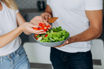 Closeup male and female hands cooking healthy food .  Man holding salad plate