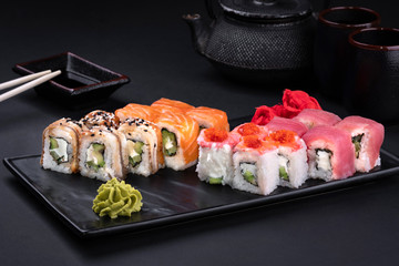 Close up Philadelphia roll sushi with salmon, avocado and cream cheese with chopsticks and soy on black background. Sushi menu. Japanese food and green tea teapot, copy space. Sashimi set.