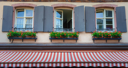 Ribeauvillé is a commune in the Haut-Rhin department in France. This town is in the historical and cultural region of Alsace.Three shuttered windows with flowers and a red and white striped awning.