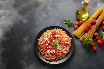 Classic Italian spaghetti pasta with tomato sauce, mozzarella, cherry tomatoes and basil on plate on dark table