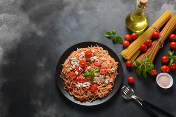 Classic Italian spaghetti pasta with tomato sauce, mozzarella, cherry tomatoes and basil on plate on dark table