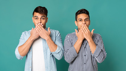 Two Surprised Men Covering Mouth With Hands Over Turquoise Background