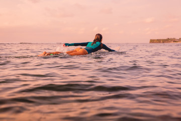 Surf girl with perfect body on surfboard in ocean. Surfing at sunset time