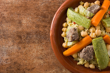 Traditional tajine with vegetables, chickpeas, meat and couscous on rusty background. Top view. Copyspace