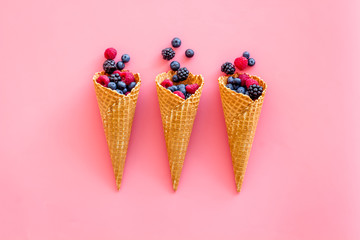 Fresh berries in waffle cones on pink background top view