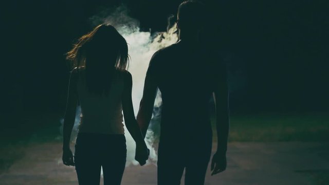The couple walking in the dark street through a white smoke. slow motion