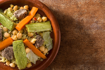 Traditional tajine with vegetables, chickpeas, meat and couscous on rusty background. Top view. Copyspace
