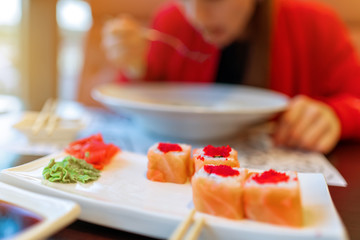 girl eating pasta and sushi, blur. without a face. lunch, meal in the restaurant. red clothes, sushi Philadelphia