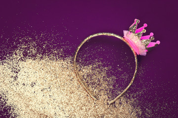 Pink and gold princess crown headband for girls on dark purple background with golden dust glitter. Festive birthday party or performance with copy space © taniasv