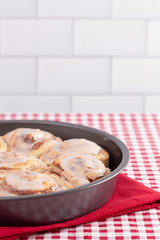 Pan of Frosted Cinnamon Rolls on a Red and White Plaid Tablecloth