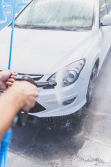 Close up of man hand washing car with pressure washer outdoors.