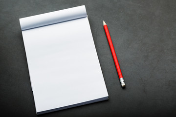 Notepad with a red pencil on a black stone plate background, for education, recording goals and deeds