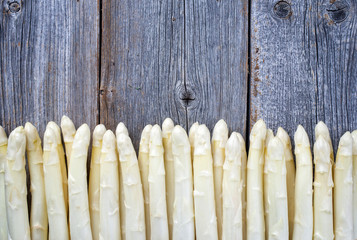 Raw white Asparagus beaded in a row on an old rustic wooden board as close-up with copy space on top