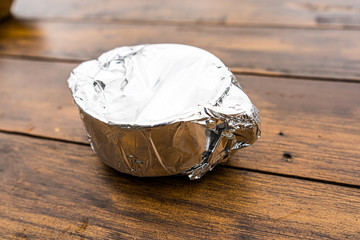 Food on a plate wrapped in foil on a plate on a wooden table outside, breakfast served at a hotel.