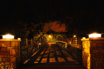 A wooden pedestrian bridge illuminated by solar lights surrounded by trees and rock wall in a nightime South Dakota landscape