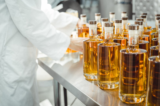 Small liquor production based on maple syrup. Lot of pure alcohol bottles unlabeled. Bottles placed in a row. Person in lab coat analyzing the bottles.