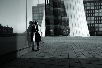 Obraz premium Black and white photo of a girl in a coat reflecting in the building against the business center
