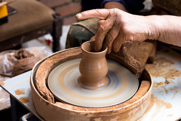 a potter (man) molding a vase of clay on a spinning potter's wheel, close up