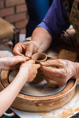 an adult potter helps a child to learn how to work with clay on a potter's wheel, forming a clay...