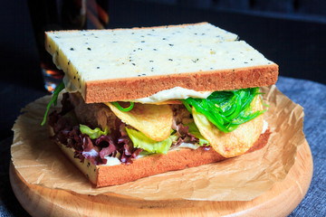 American fast food. Juicy tuna sandwich with chips, lettuce on a dark background. Club food.